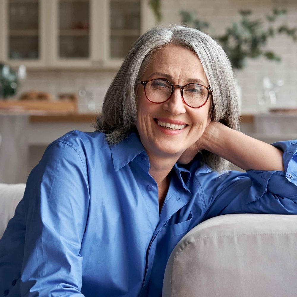 Happy relaxed mature old woman wears glasses sitting on couch at home, portrait.