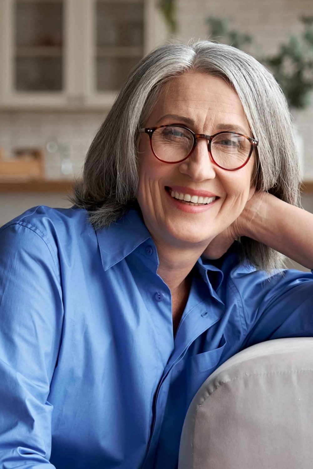 Happy relaxed mature old woman wears glasses sitting on couch at home, portrait.