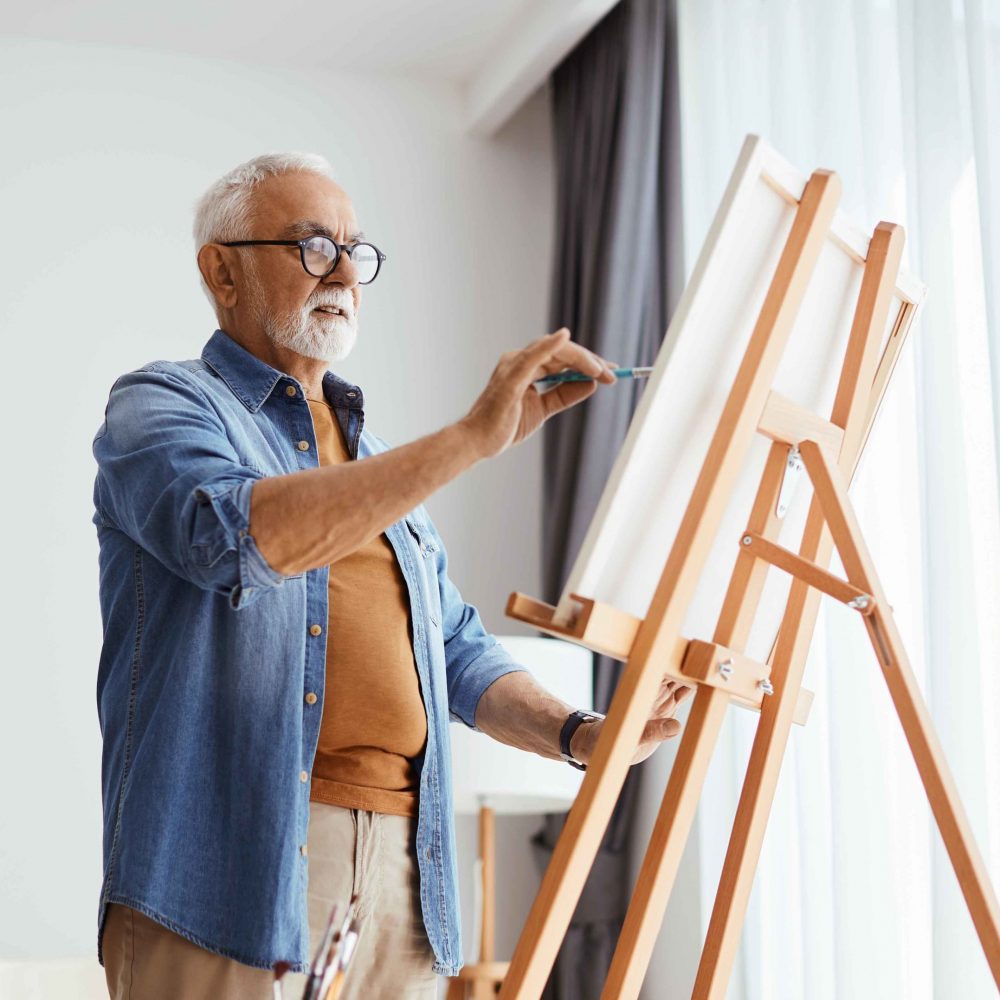 Senior man painting on canvas while enjoying creative time at home.